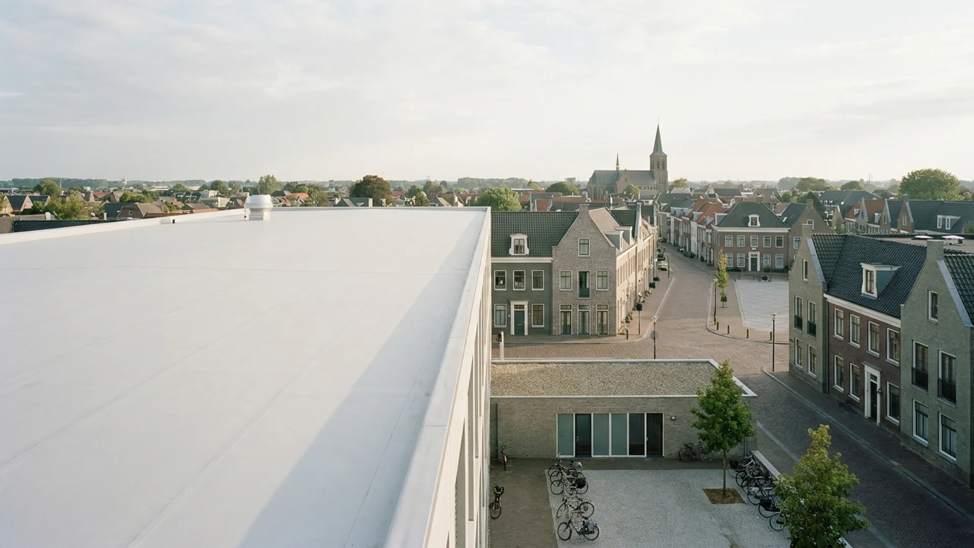 Wit gecoat dak van een gemeentelijk gebouw met een Nederlands dorpscentrum erachter
