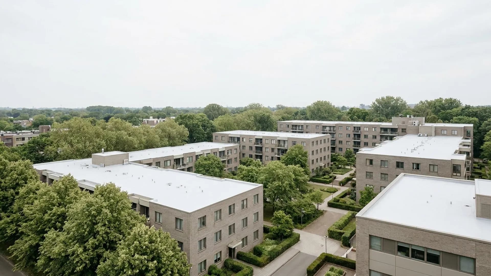 Meerdere wit gecoate daken van appartementenblokken tussen het groen